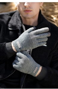 Detail of grey knitted gloves with a branded label against a rustic hay background