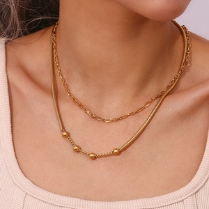 Detailed view of a layered gold snake chain necklace with beads on female model