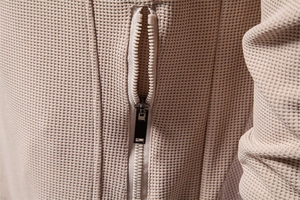 Macro detail of high-quality waffle texture fabric and metal zipper on beige casual jacket