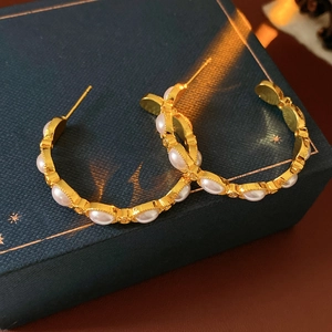 Dettaglio di orecchini a cerchio vintage dorati con perle e trama intrecciata su box