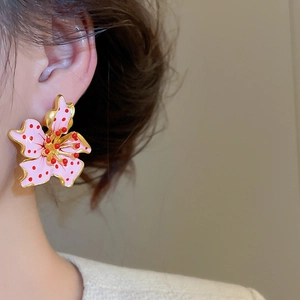 Close-up of pink flower earrings with gold edges worn by a model in a minimal setting