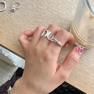 Detail of silver knot letter ring on hand with lifestyle background and coffee cup
