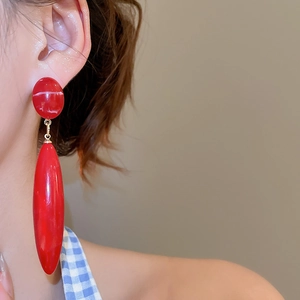 Close-up of long red acrylic waterdrop earrings with gold metal accents on a model