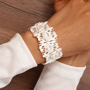 Detailed view of wide silver bangle with floral relief texture worn on a female wrist