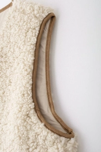 Gros plan du col du gilet en polaire beige avec bordure en daim marron contrastant