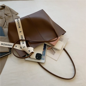 Brown large capacity leather tote bag with stylish wide canvas strap on white bedding