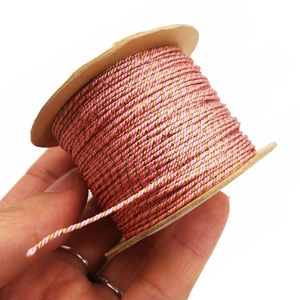 Hand holding pink and gold braided 1mm cord wound on a kraft paper coil roll