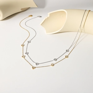 18k gold and silver heart-shaped pendant necklaces with cubic zirconia on white stone stand