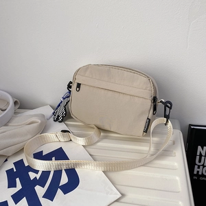 Detail of beige nylon crossbody bag with fashion label and checkerboard charm on a white surface
