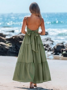 Groene backless maxi-jurk met ruches en grote strik tegen een stranddecor
