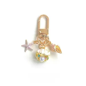 Detail of a gold starfish, seashell with pearl and conch pendant on a keychain