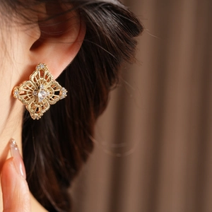 Macro view of gold hollow flower earrings with sparkling zircons on a model's ear