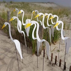 Outdoor scene of white egret whirligig wind spinners decorating a sandy beach garden