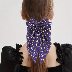 Detail of a large purple satin bow hair clip with yellow moon and star prints for parties