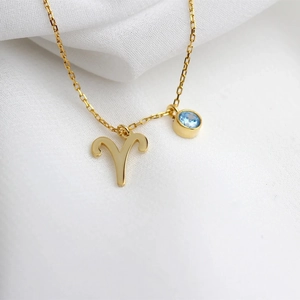 Macro shot of gold Aries zodiac necklace with blue zircon and rune pendant charm