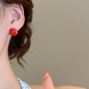 Close-up of red apple-shaped stud earring with silver star detail on model's ear