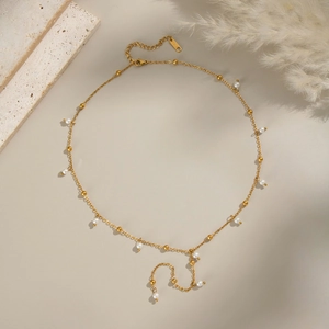 Elegante collana a Y dorata con piccole perle bianche su una catena di metallo minimale