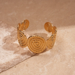 Gros plan du bracelet jonc doré avec gravure en spirale sur une surface en pierre