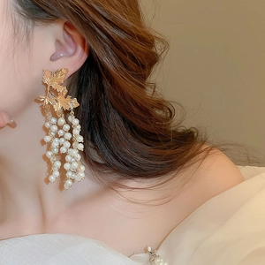 Detail of golden maple leaf earrings with white pearl tassels on a female model