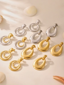 Detailed view of polished gold and silver geometric hoop earrings on a sandy background