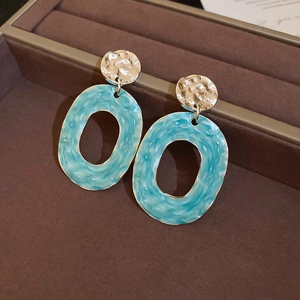 Close-up of sky blue enamel earrings with textured silver oval pendants in a jewelry box