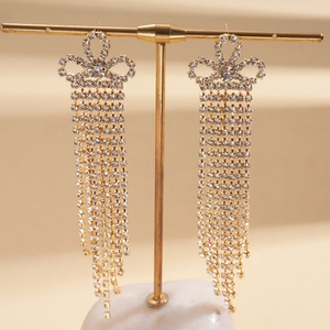 Vue détaillée de longues boucles d'oreilles dorées à pompons avec strass sur un support