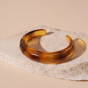 Detail view of amber acrylic resin irregular open bangle on natural stone base