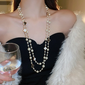 Double-layered gold pearl necklace with black and white clover charms on a female model