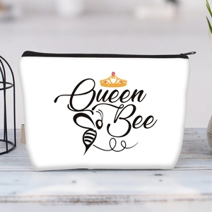 Detail of white canvas makeup bag with Queen Bee print and gold crown on a wooden table