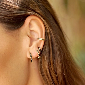 Close-up of model wearing gold ear hoops and cuffs with inlaid black zircon stones