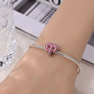 Macro view of silver snake chain bracelet with pink enamel zodiac charm and stones