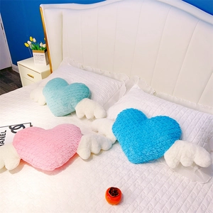 Gros plan de coussins en peluche en forme de cœur avec ailes en rose et bleu sur lit