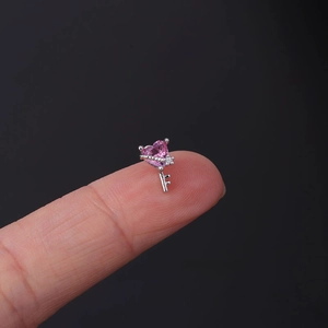 Macro shot of 20G stainless steel pink heart key stud earring held against a fingertip