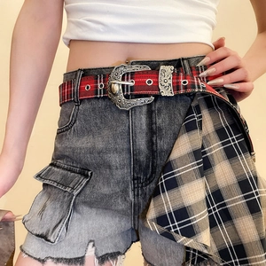 Detail of red tartan fabric belt with western floral engraved metal buckle on denim