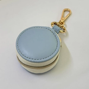 Close-up of mini round blue leather jewelry case with gold metal carabiner and white zipper