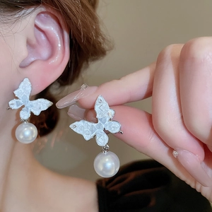 Gros plan de boucles d'oreilles papillon avec texture coquillage et perles blanches