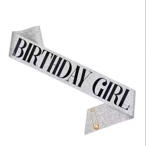Close-up of silver glitter Birthday Girl sash with black lettering and a gold safety pin