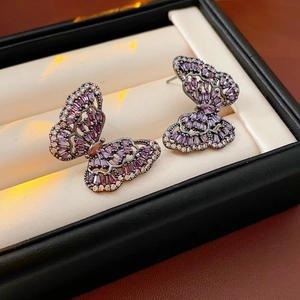 Macro detail of butterfly earrings with purple zircon stones on a white jewelry cushion