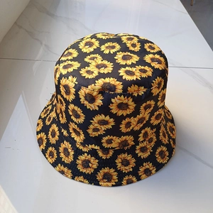 Flat lay of a black sun hat with sunflower print on white marble background