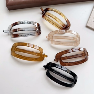 Flat lay of oval resin hair clips in amber, black, and beige on a clean white desk