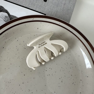 Detailed macro view of cream white hair claw clip with black text on a ceramic plate