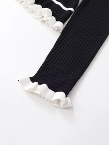 Detailed macro shot of rib-knit sleeves with white ruffle cuffs and pointelle knit accents
