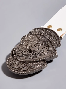 Detail of white leather belt featuring a vintage bronze carved double heart buckle