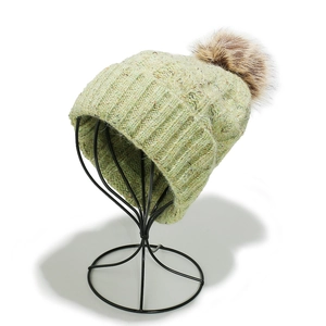 Close-up of light green ribbed knit beanie featuring a fluffy brown faux fur pompom detail