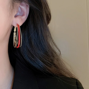 Detailed close-up of a model wearing red and gold multilayer enamel oval hoop earrings