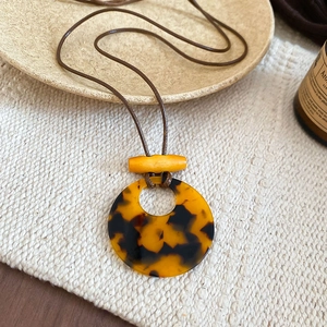 Macro shot of resin tortoiseshell pendant necklace on rustic linen with yellow wood detail
