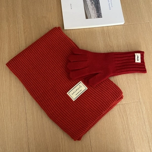 Detalle de bufanda y guantes de punto rojo con etiqueta en suelo de madera clara