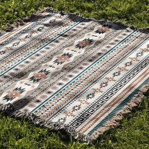 Detailed view of bohemian woven blanket with geometric patterns and fringe on green grass