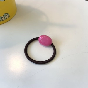 Detailed shot of elastic black hair tie with a pink oval resin bead on a white surface