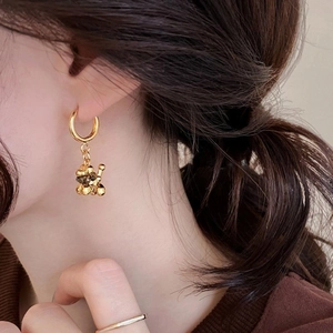 Detailed close-up of golden balloon bear earring with tiger eye stone tassel on model